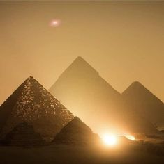 three pyramids in the desert at sunset with light coming from behind them and sun shining through