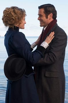 a man and woman standing next to each other near the ocean with their arms around each other