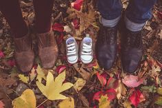 three people standing next to each other in front of leaves on the ground with their feet up