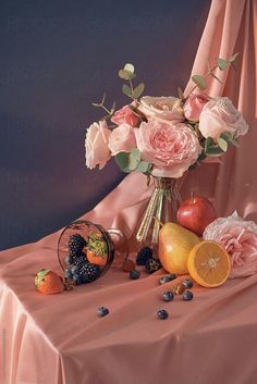 a vase filled with flowers and fruit sitting on top of a pink cloth covered table