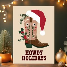 a christmas card with a cowboy boot and holly wreath on it, sitting next to a pine tree