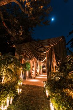 an outdoor wedding venue at night with lit candles in the grass and draped curtains on either side