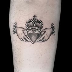 a black and white photo of two hands holding a heart with crown on it's arm