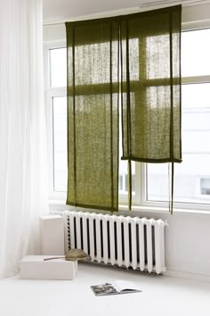 a green curtain hanging over a radiator next to a window with white curtains