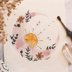 a drawing of the moon with flowers and leaves on it next to some paintbrushes