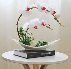 a white vase with red and white flowers on top of a table next to a book