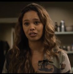 a woman with long curly hair standing in front of a shelf filled with bottles and other items