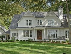 a large white house with lots of windows and trees in the front yard, surrounded by lush green grass