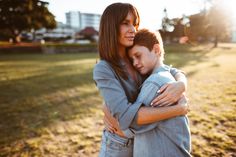 a woman hugging a young boy in a park at sunset or early morning with buildings in the background