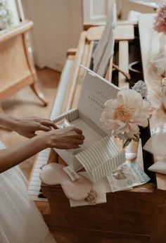 a woman is opening a gift box with flowers on the table in front of her