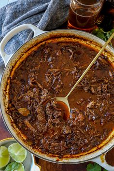 a large pot filled with beef and sauce on top of a wooden table next to limes