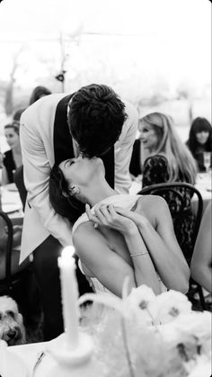 a man kissing a woman on the cheek in front of a table full of people