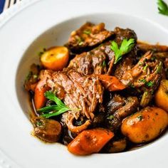 a white bowl filled with meat and vegetables on top of a table next to utensils