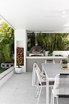 an outdoor kitchen and dining area with wood burning oven in the back ground, surrounded by greenery