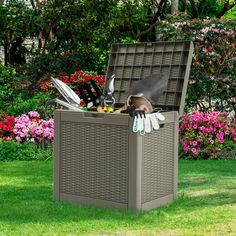 an outdoor storage box with gardening utensils in it on the grass near flowers