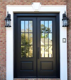 a black double door with two sidelights on the brick wall and white trim around it