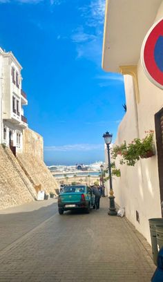 a blue car is parked on the street next to a white wall and some buildings