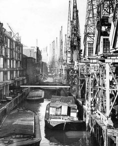 an old black and white photo of boats docked in the water near some construction cranes