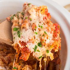 a wooden spoon full of lasagna casserole being lifted from a white bowl