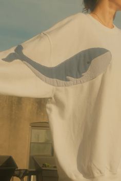 a woman wearing a white shirt with a whale on it's back and her hands in her pockets