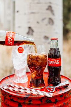 coca - cola is being poured into two glasses on an old metal tray with ice