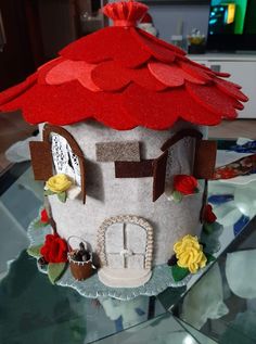 a cake shaped like a house with red roof and flowers on the bottom tier, sitting on a glass table