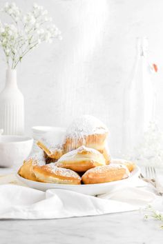 powdered sugar covered donuts on a white plate with flowers in the back ground