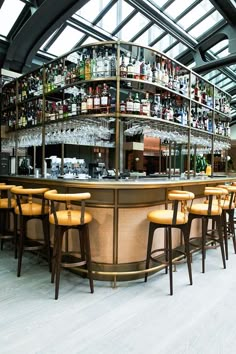 a bar with yellow chairs and bottles on the top shelf, in front of an arched glass ceiling