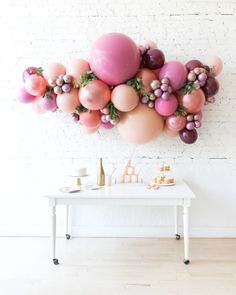 a white table topped with lots of pink and gold balloons next to a wall mounted balloon art