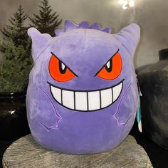 a purple stuffed animal with orange eyes and fangs on it's face sitting on a tree stump