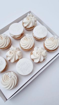 twelve cupcakes with white frosting in a card board box on a table