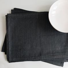 a white bowl sitting on top of a table next to two black cloth napkins