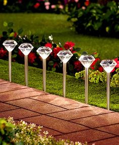 five diamond shaped lights are lined up on the side of a brick path in front of flowers