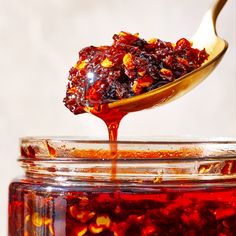 a spoon full of jelly sitting on top of a jar filled with liquid and nuts