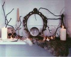 candles are lit on a mantle with branches around it and an ornate mirror in the middle