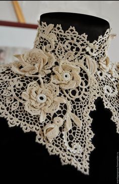 a white lace scarf with flowers and pearls on it's edge, hanging from a black mannequin