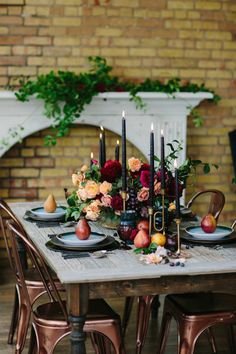 the table is set with candles, fruit and flowers in front of a brick wall