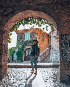 a woman standing under an archway in the middle of a stone building with ivy growing on it