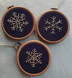 three embroidered snowflakes are hanging from wooden hoop holders on a blue tablecloth