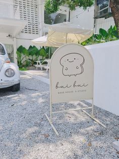 a white sign sitting on top of a gravel covered parking lot next to a parked car