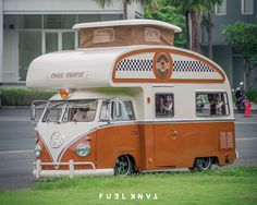 an orange and white camper parked in the grass next to a street with palm trees