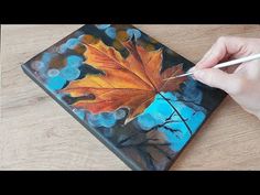 someone is painting an autumn leaf on a piece of wood with acrylic paint