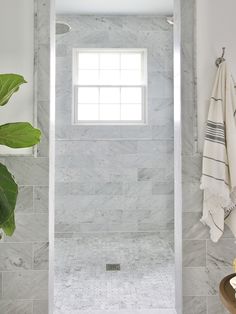 a white bathroom with marble tile walls and floor, along with a window in the corner