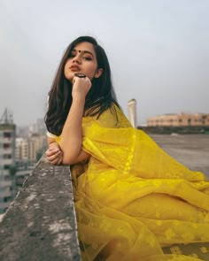 a woman in a yellow dress leaning on a wall with her hand to her mouth