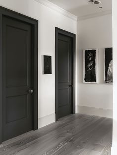 an empty room with two black doors and pictures on the wall above them, along with hardwood flooring