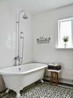 a white bath tub sitting under a window next to a stool and potted plant