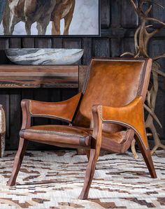 a brown leather chair sitting in front of a painting on a wooden wall next to a table