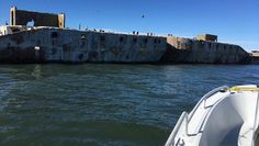 a boat is in the water next to an old concrete structure with birds flying over it