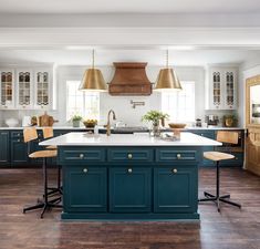 a large kitchen with blue cabinets and wooden flooring, two pendant lights hanging over the island