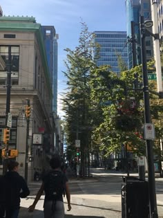 two people are walking down the street in front of some tall buildings and trees on both sides